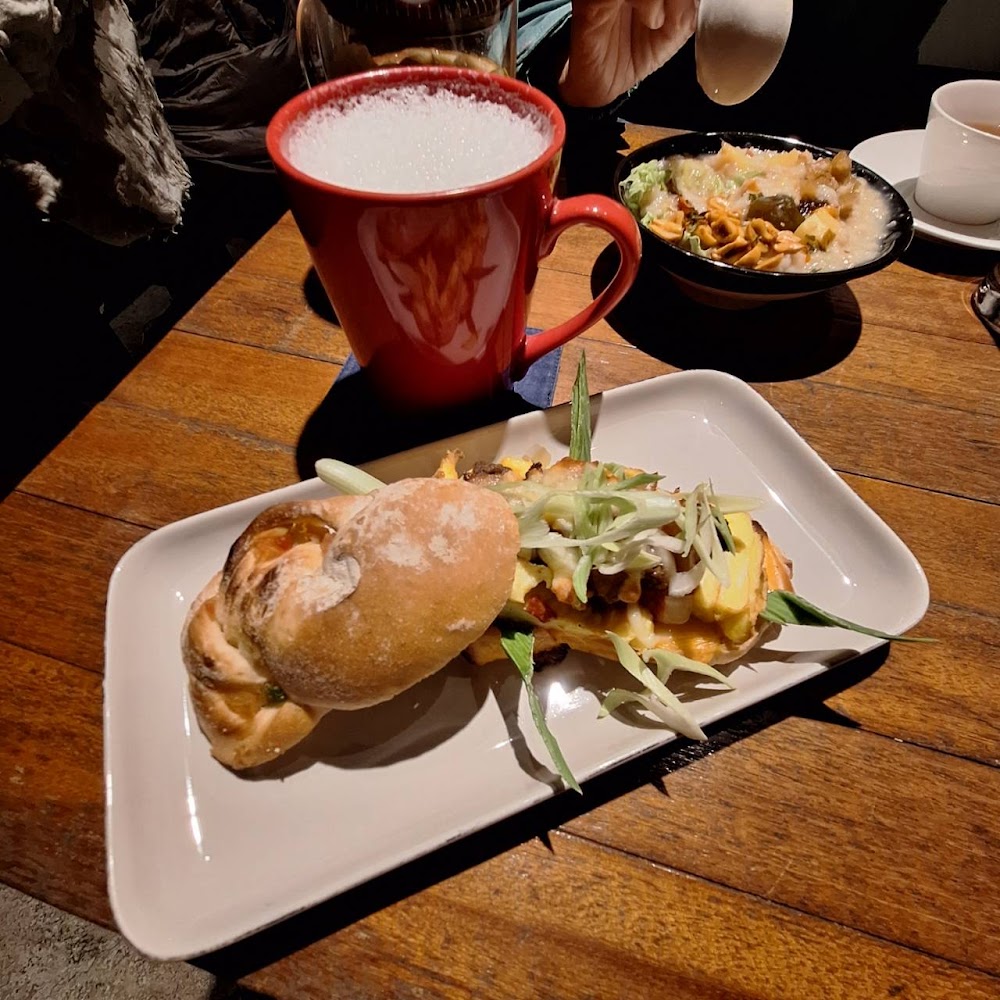 這張圖片主要有一杯奶泡飲品、兩種麵包、以及一盤含多種配料的主食，擺放在木質餐桌上，整體呈現豐盛的早午餐氛圍。