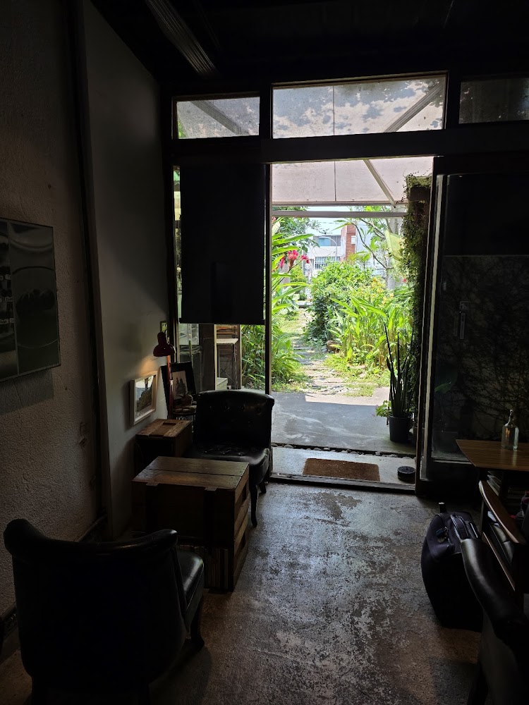 這張圖片展示一間有開放式出口的室內空間，內有兩張皮椅、一張木桌，還有不少植物裝飾，門外是綠意盎然的花園小徑，整體氛圍悠閒自然。