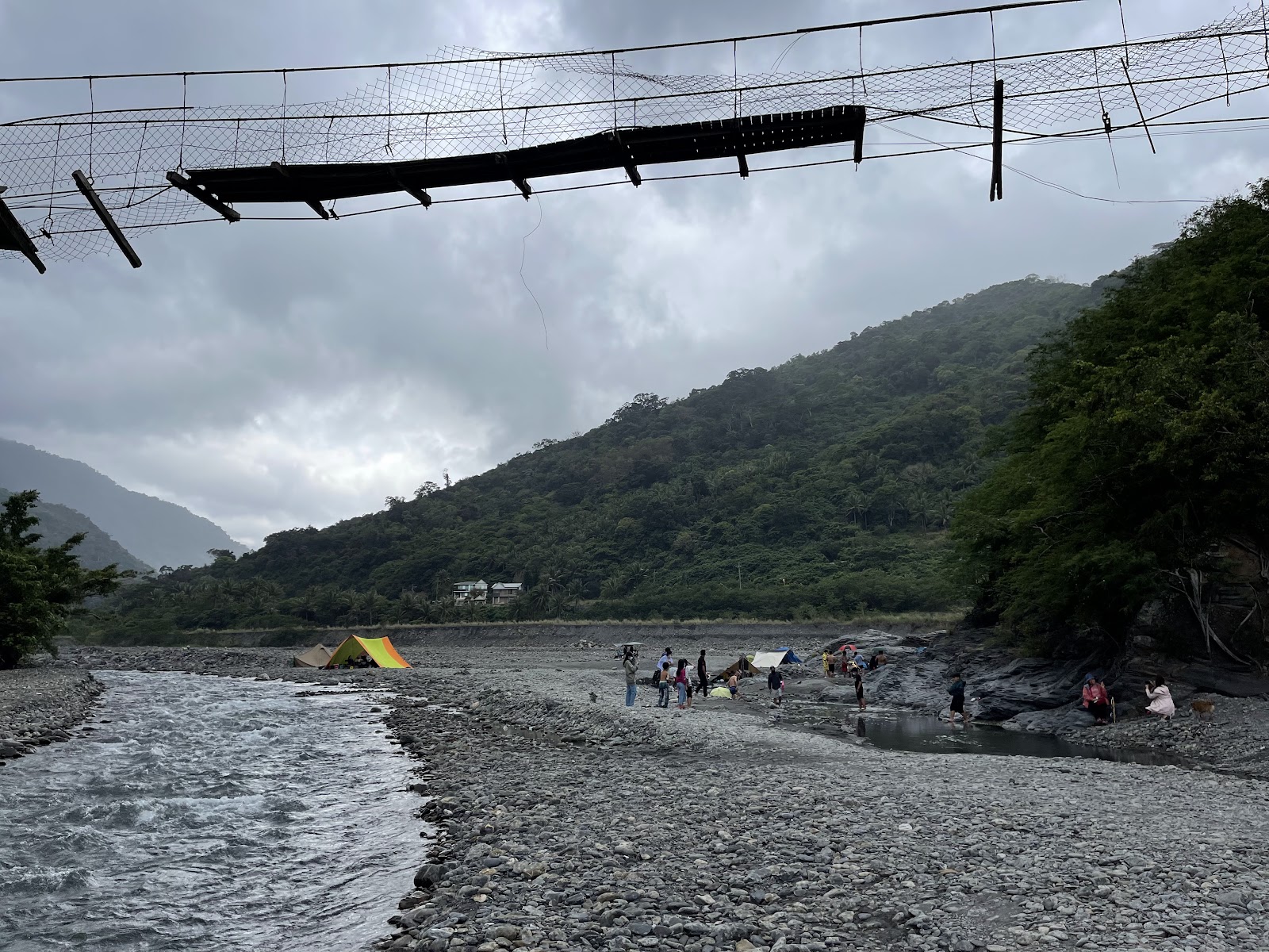 從金崙溪吊橋俯視溪床,遊客在礫石灘搭起彩色帳篷露營,遠景是環繞的青山