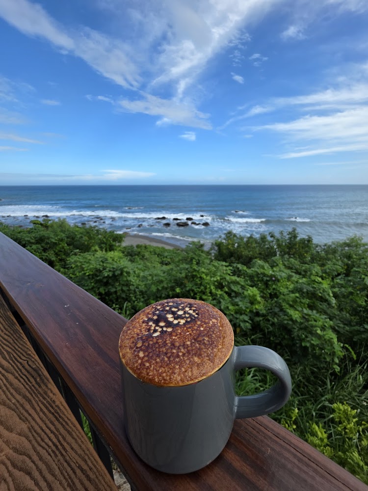 有焦糖奶泡的咖啡杯，放在欄杆上，背景是藍天白雲和壯麗的海邊景色