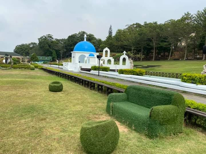 這張圖片主要有一座藍白色圓頂建築，周圍景觀綠意盎然，前景有以人工草皮包覆的椅子和圓形坐墊，整體環境清新悠閒。