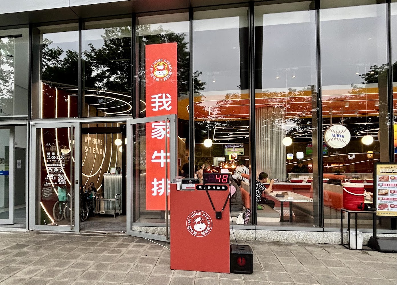 我家牛排板橋遠科旗艦店外觀有紅色招牌與取號機