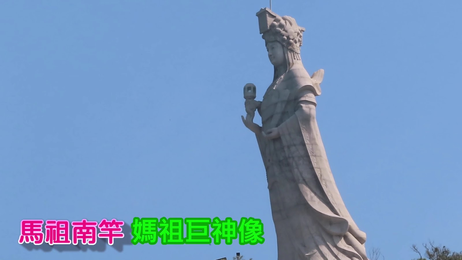 媽祖巨神像仰角近景，神像持燈籠側面細節，藍天背景