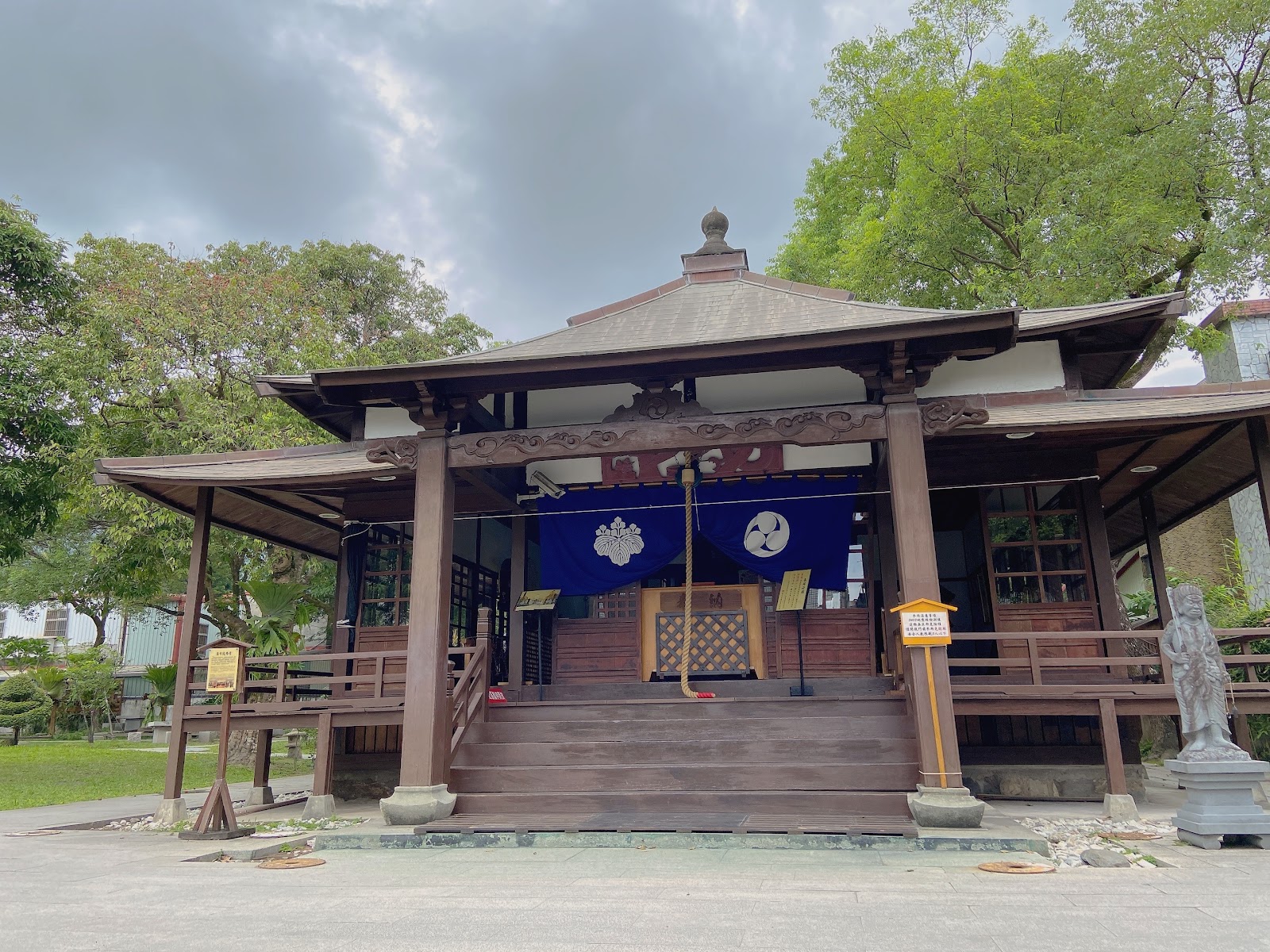 吉安慶修院本堂廣角全景，棕色木造廊殿，藍色家紋布幕，石獅守護，大樹環繞