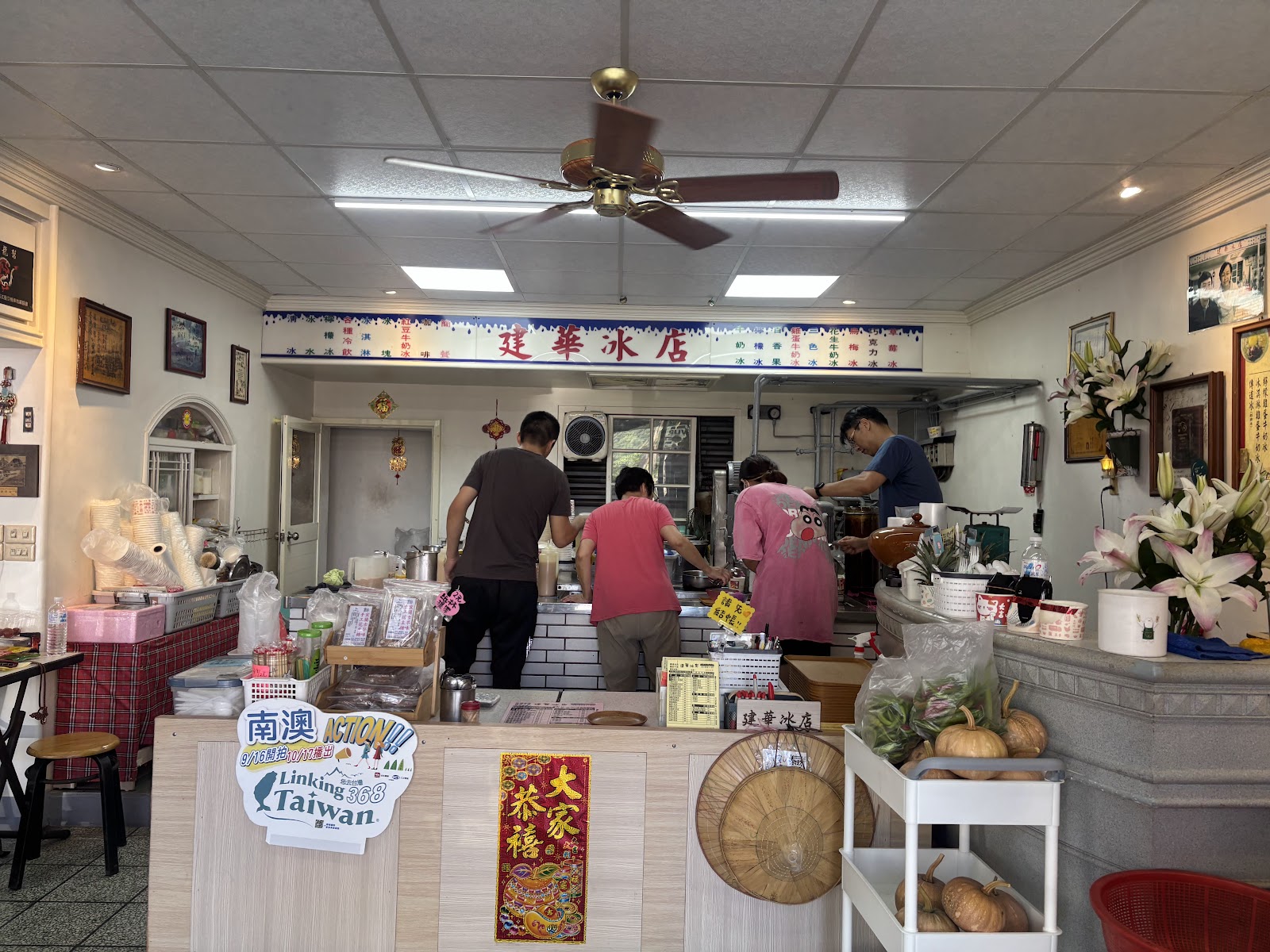 建華冰店店內全景，工作人員正在備料，牆面貼滿老照片與獎狀