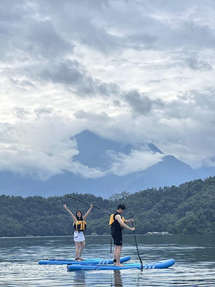 兩人在湖面上站立划槳板，背景有青山和雲霧