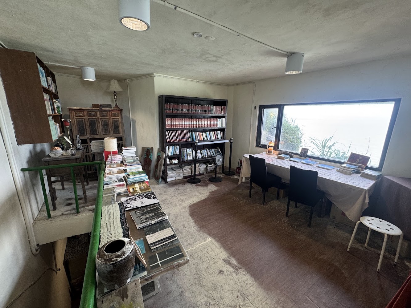 這張圖片展示了一間書房或閱讀空間，內有書架、桌子、椅子和大量書籍。大窗戶外可見自然景色，空間布置溫馨安靜，適合閱讀或寫作。