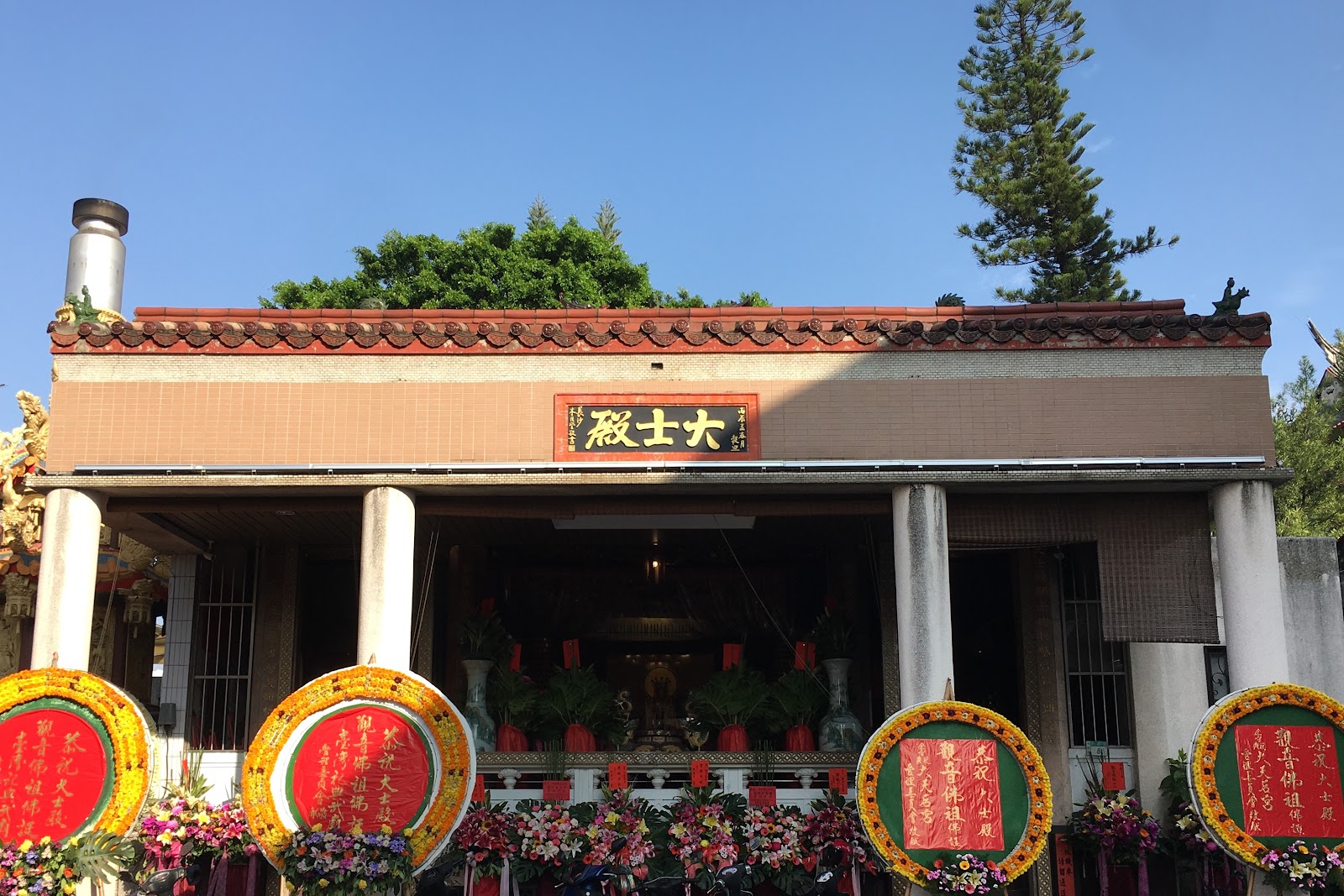 赤嵌樓大士殿廟殿外觀,牌匾莊嚴,前有花圈供品整齊排列,晴天藍天