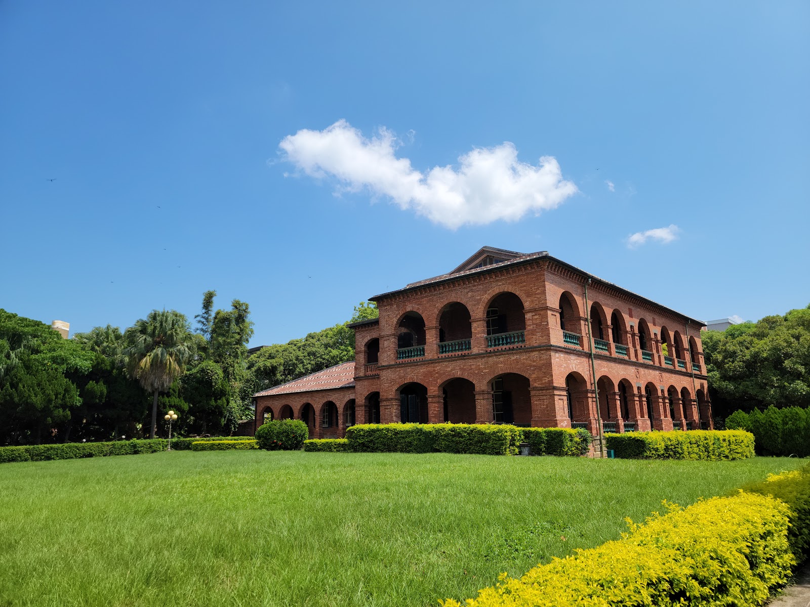淡水紅毛城遠景，前方綠色草坪，紅磚建築配合藍天白雲