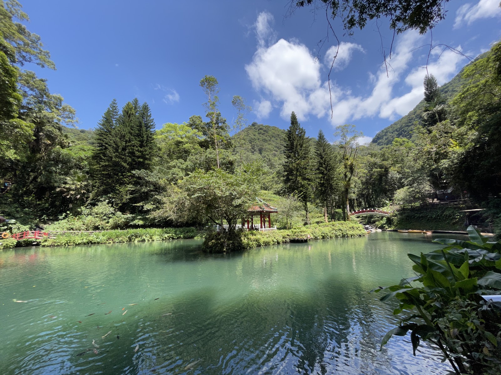 翡翠綠湖中央涼亭，四周翠綠山林，藍天白雲倒映水面