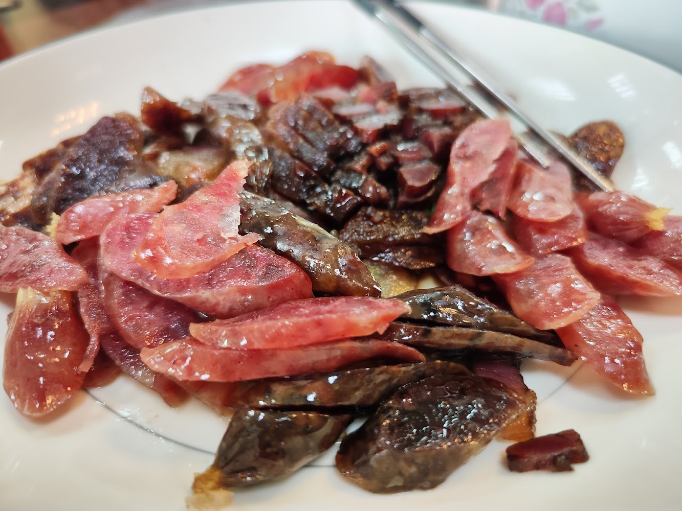 一盤切片的臘腸與臘肉，看起來油亮可口，擺放在白色餐盤中