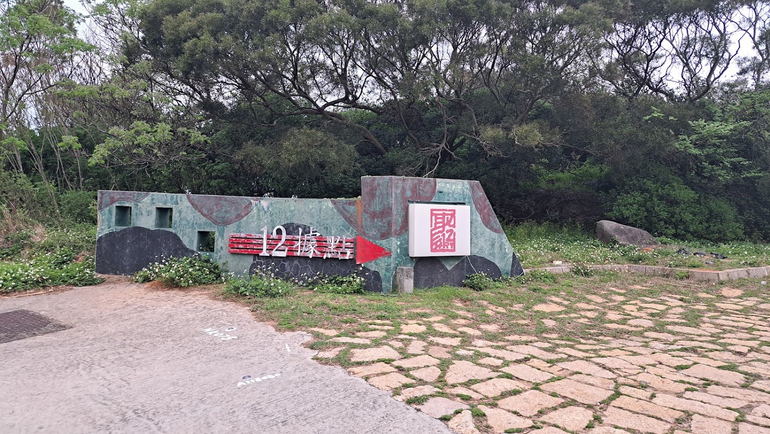 這張圖片主要是一處名為『12據點』的軍事遺址指標，標誌及周圍有茂密的樹木和花草，營造出濃厚的歷史與自然氛圍。