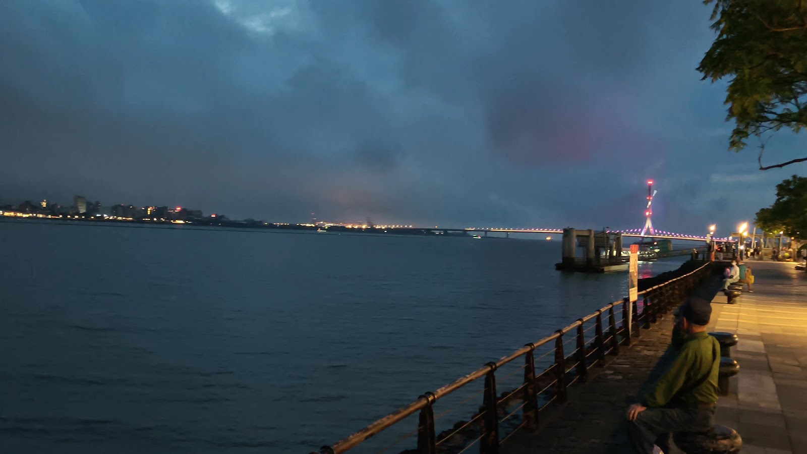 淡水河岸夜景，橋燈紅光，遊客散步，遠眺觀音山燈光