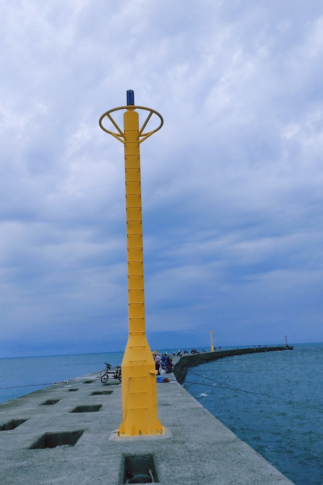 海邊防波堤上的黃色燈塔與遠方釣客