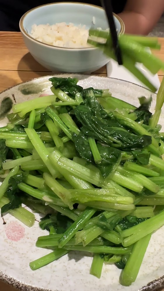 一盤炒青菜搭配白飯，有人用筷子夾起青菜。