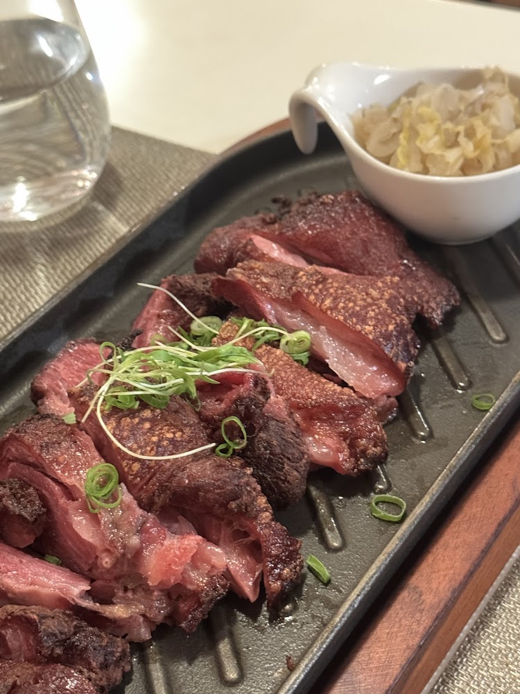 一盤切片牛排，表皮酥脆、肉質多汁，上面撒有蔥花，旁邊有一小碟配菜