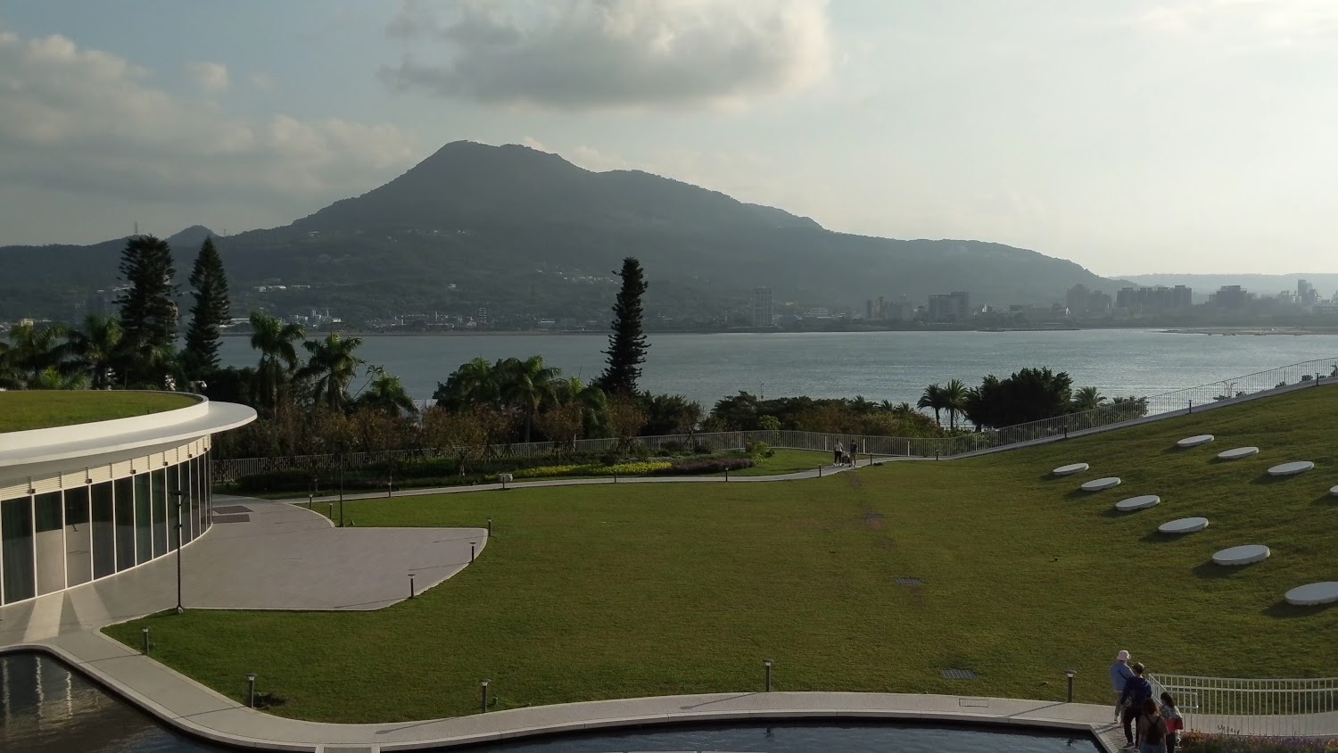 滬尾藝文休閒園區大片草地池塘與遠方河流山景