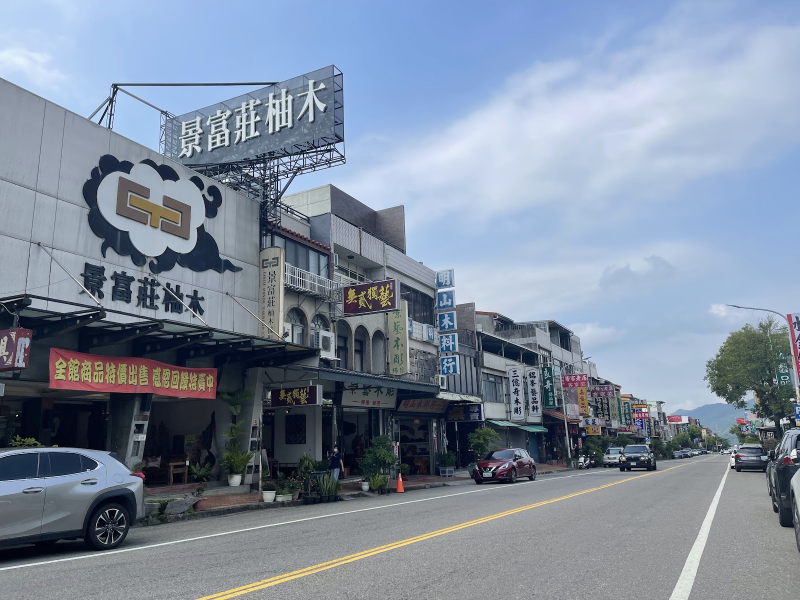 三義木雕街商店景觀，兩側木雕藝品店林立，藍天白雲