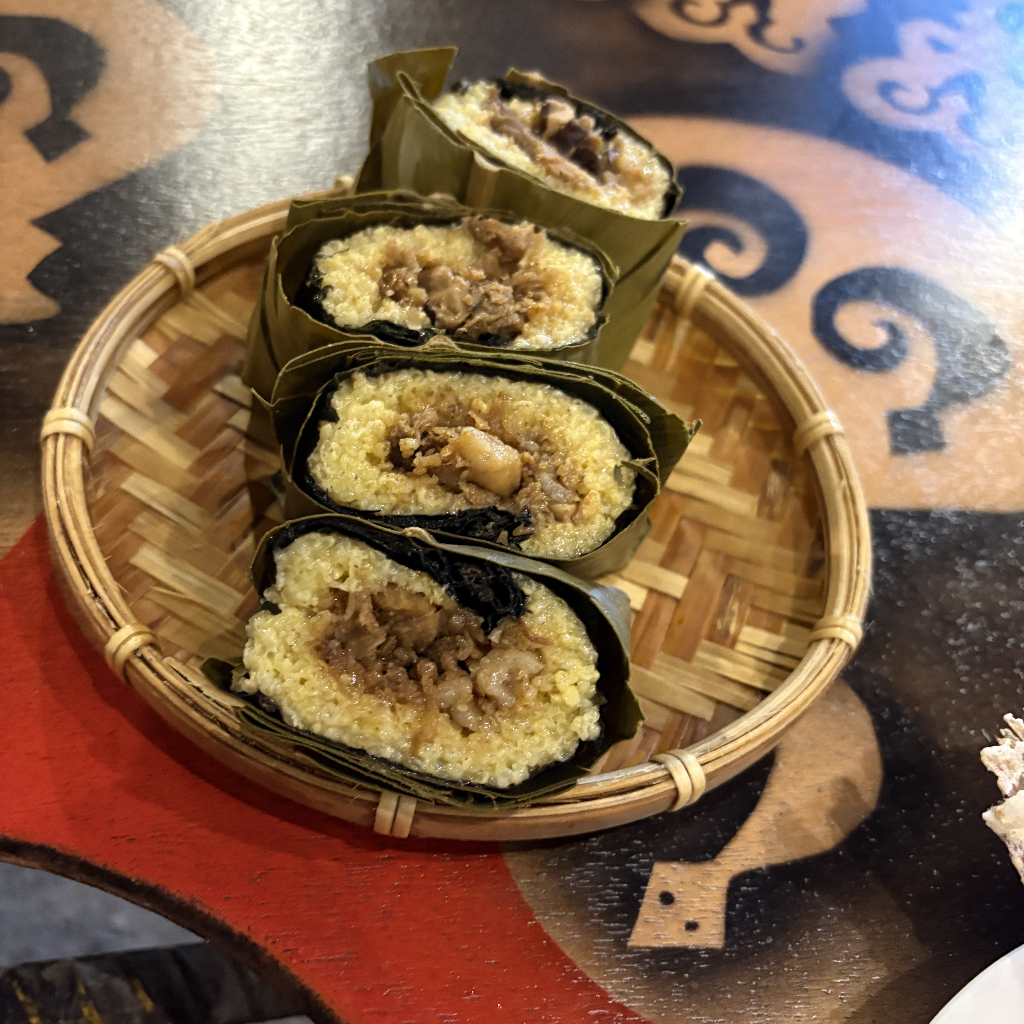 四塊放在竹編托盤裡的糯米飯捲，外圍以葉子包裹，內餡有肉類及醬料
