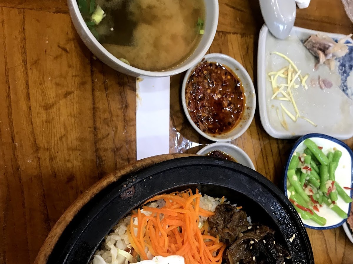 十一街朝鮮拌飯，黑色石鍋盛飯，配胡蘿蔔絲、木耳、豆芽、荷包蛋，旁有湯和小菜