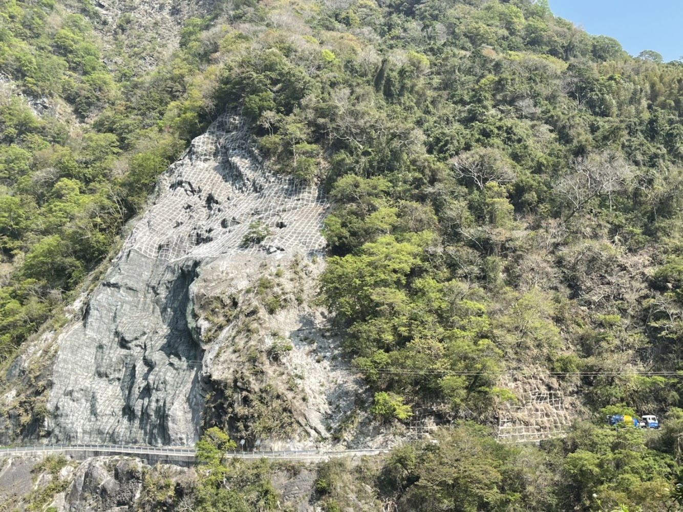 陡峭山坡覆蓋防護網下方有小路與車輛