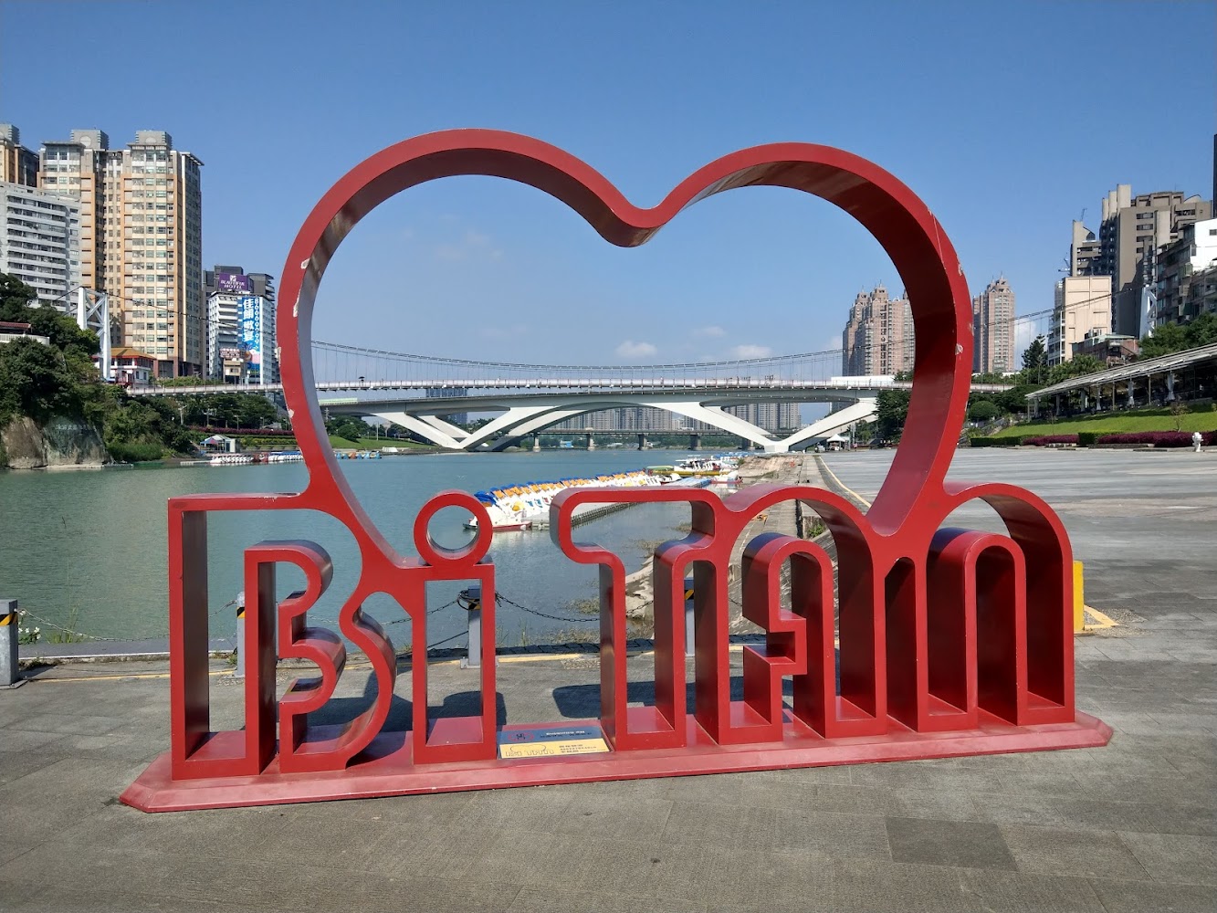 紅色愛心造型裝置藝術寫著 Bitan，背景是河流橋樑與高樓