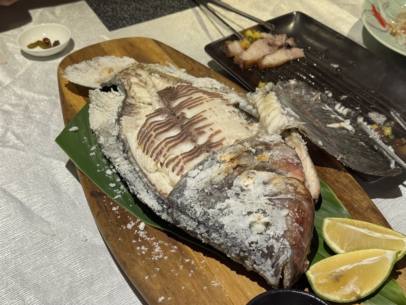 木盤上的鹽烤魚，魚身覆蓋厚鹽，搭配檸檬片和配菜