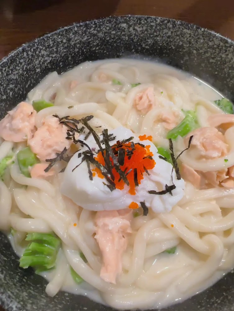 這張圖片主要是一碗濃湯烏龍麵，上面有鮭魚塊、溫泉蛋、蔬菜、魚卵和海苔絲，看起來非常豐富美味。