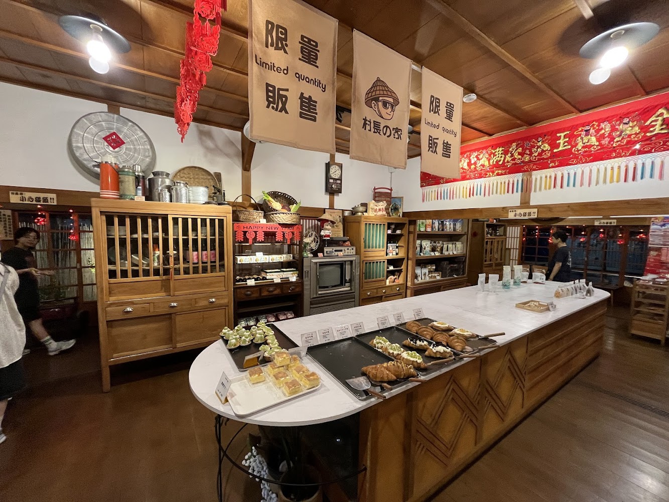 復古風甜點店內部，中央長桌陳列甜點，牆面掛有布旗與新年裝飾