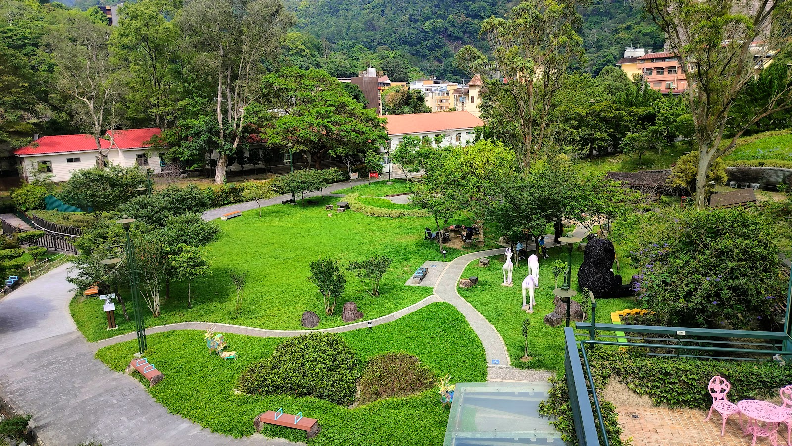谷關公園高處俯瞰,翠綠大草坪,白色鹿形雕塑,蜿蜒步道,遠山和彩色度假建築