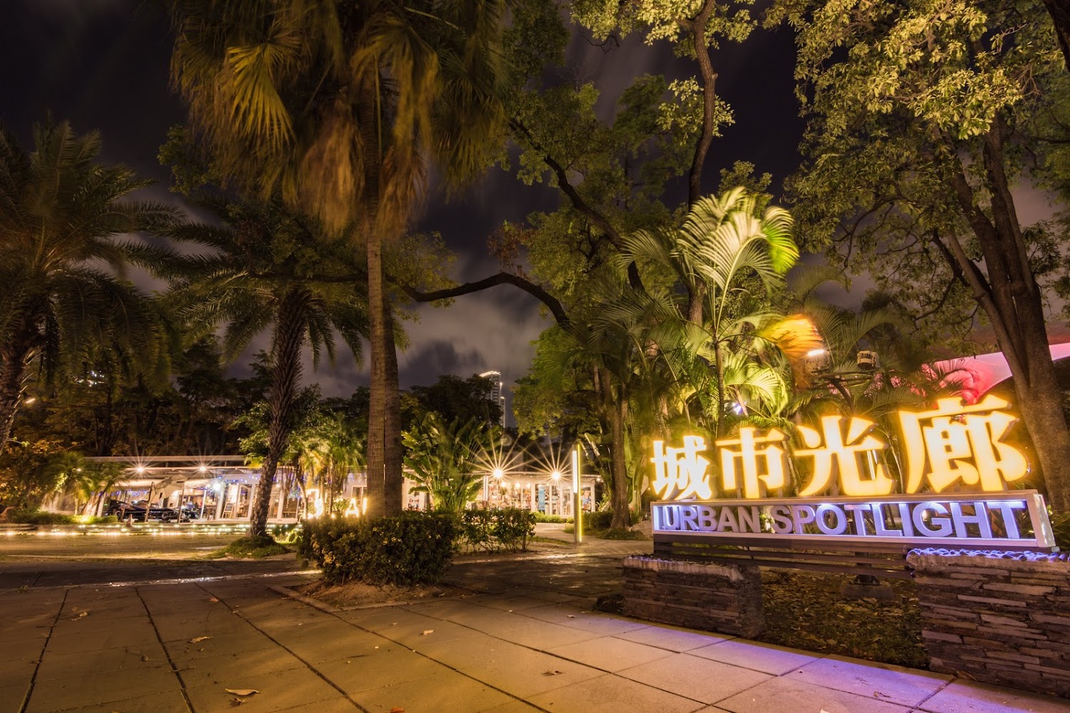夜晚都市公園入口處有城市光廊招牌與植栽燈光。