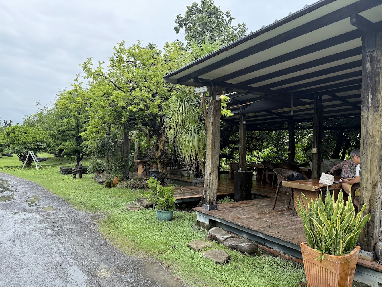 戶外木造涼亭 surrounded by trees，有人在休息喝飲料的景象