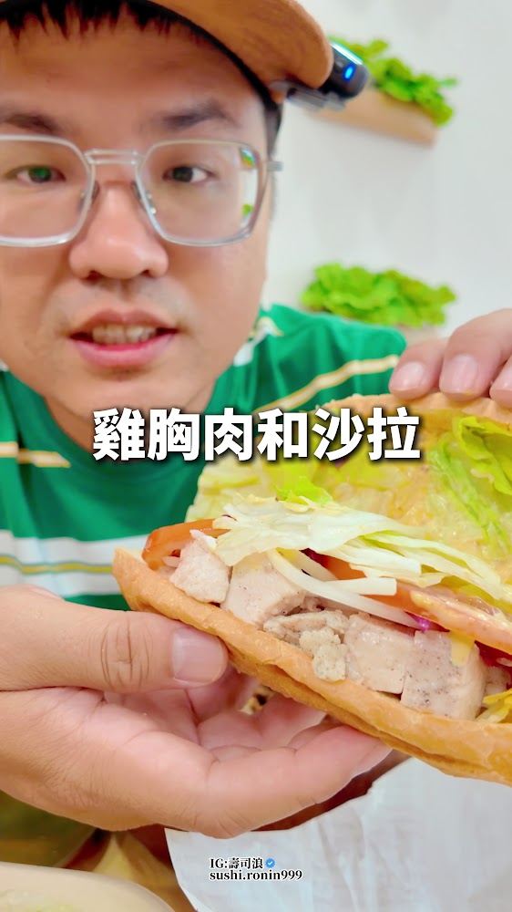 這張圖片主要展示一個人正在介紹雞胸肉和沙拉三明治，三明治裡面有雞胸肉塊、新鮮蔬菜和生菜。圖片上有文字標示其內容，背景擺放著一些蔬菜裝飾。