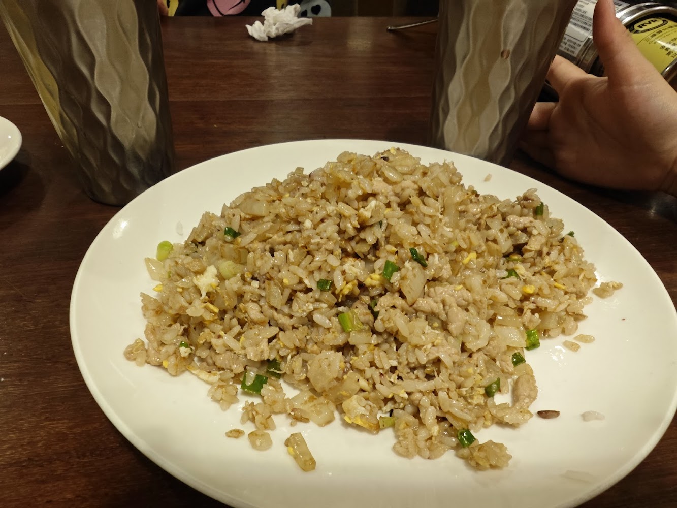 這張圖片主要是一盤炒飯，炒飯裡有蛋、青蔥和肉絲。桌上還有兩個飲料杯，以及一隻手拿著罐裝飲料。