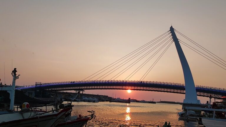 淡水情人橋夕陽剪影，橋身倒映水面，金光燦爛