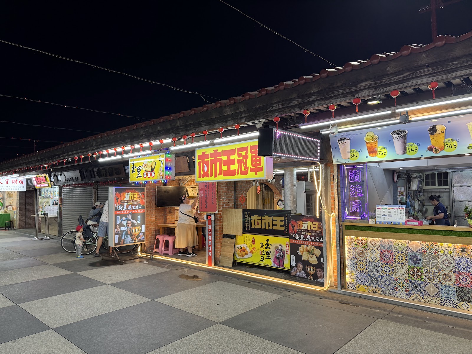 東大門夜市夜晚攤位燈火通明，紅燈籠高掛方格地磚步道