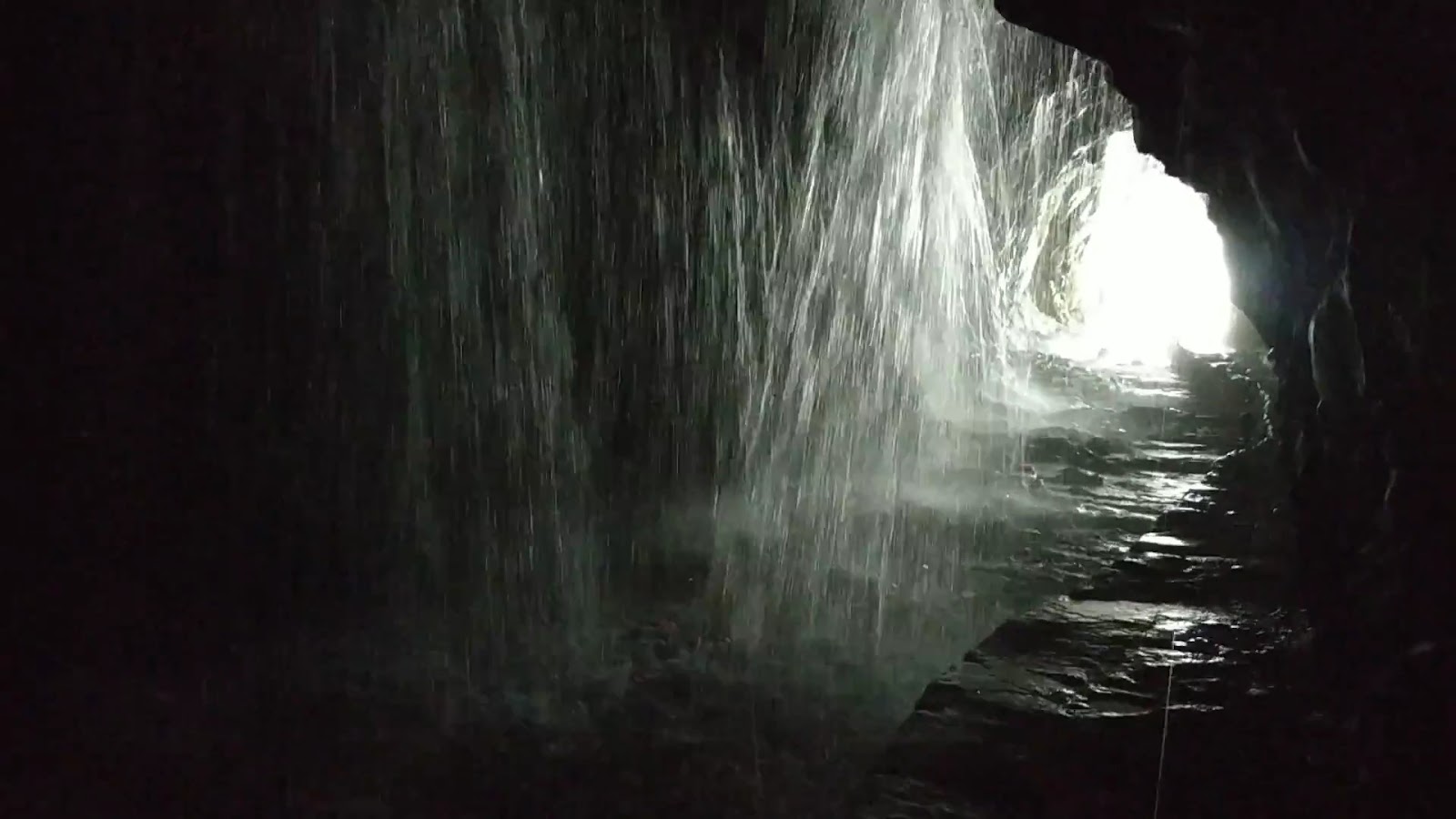 白楊步道水簾洞內部，大量水流從岩壁縫隙傾瀉而下如簾幕，洞口透出一道白光，神秘壯觀