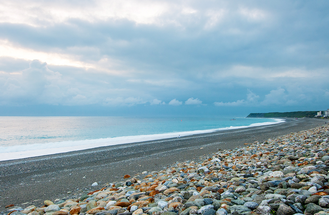 五顏六色鵝卵石海灘海浪與厚重雲層