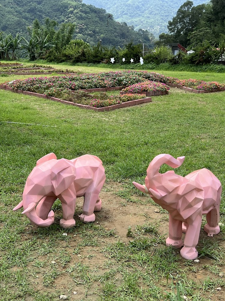 兩隻粉紅色大象造型雕塑前方是綠色草地,後方是花圃和樹木