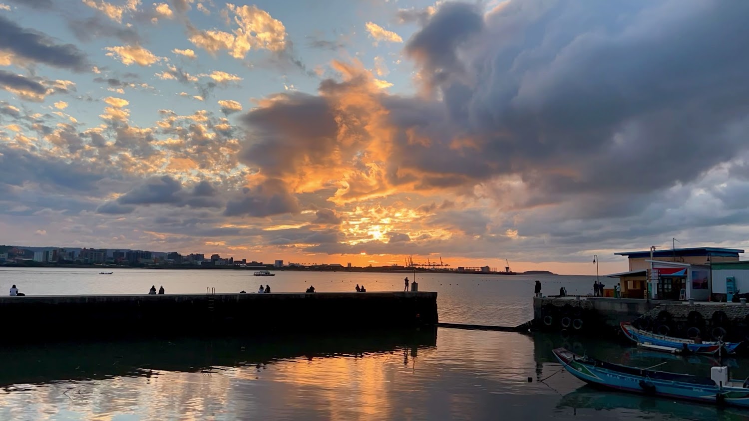 海港夕陽美景，金黃色天空下有小船與看景的人們