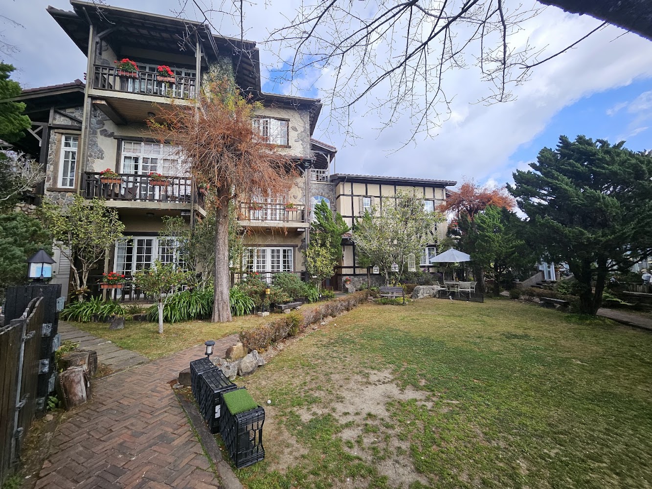 三層樓歐式房屋前方有庭院綠草與露天座椅陽傘