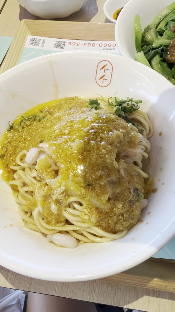 拌麵近拍，麵條粗彈，上面覆蓋金黃色醬汁與蔥花。