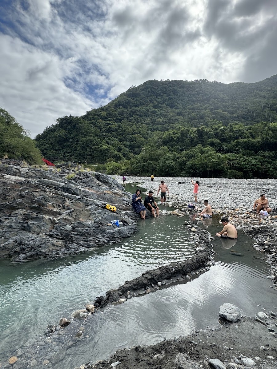 遊客在金崙野溪溫泉泡湯,岩石溪床間的天然熱湯,背景是青山藍天