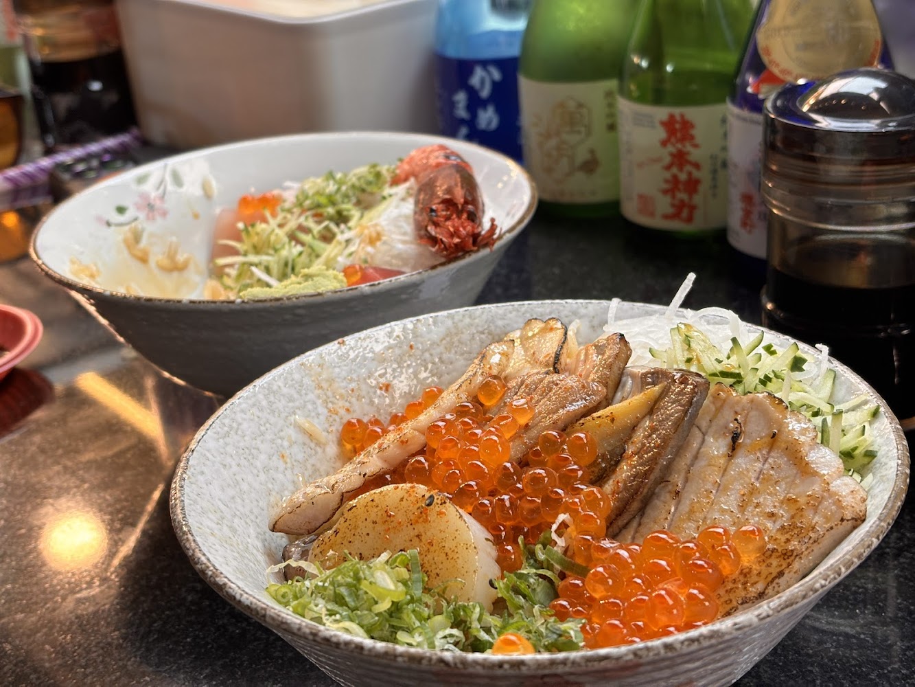 魚莊海鮮丼飯兩碗與清酒瓶背景