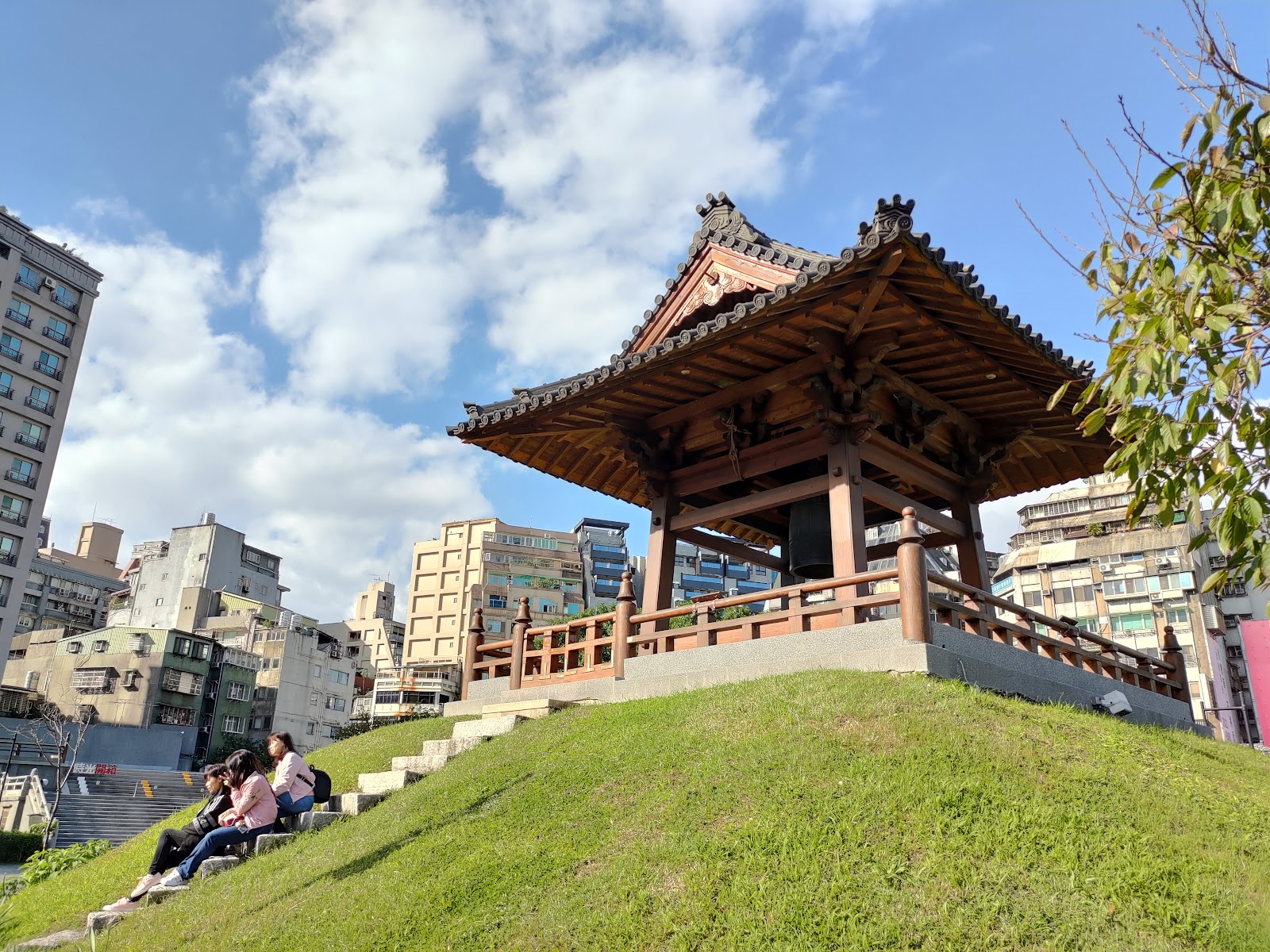 西本願寺廣場木造日式亭台，翠綠草坪，石階上坐著遊客，藍天白雲背景
