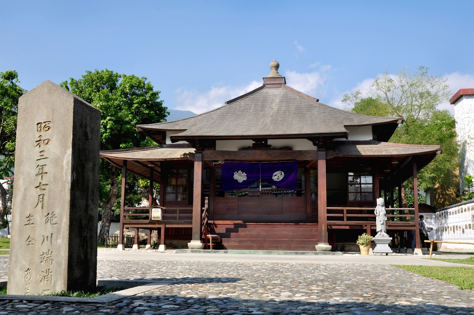 吉安慶修院本堂全景，昭和石碑、觀音像、鵝卵石步道與藍色布幕