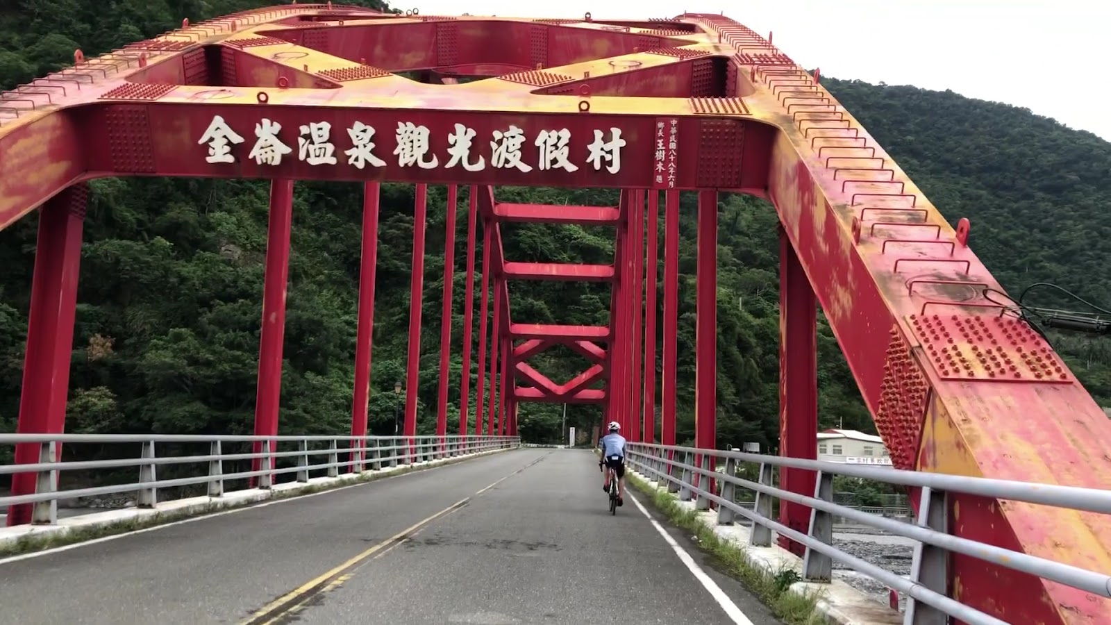金崙溫泉虹橋橋面仰視,金崙溫泉觀光渡假村字樣清晰,騎士正穿越橋面,背景青山
