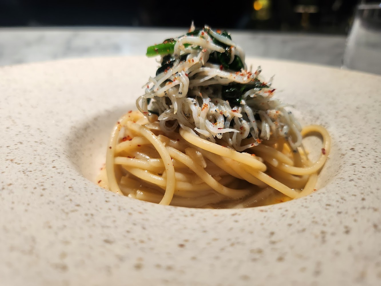 義大利麵上有白色小魚與青菜點綴，外觀精巧美味