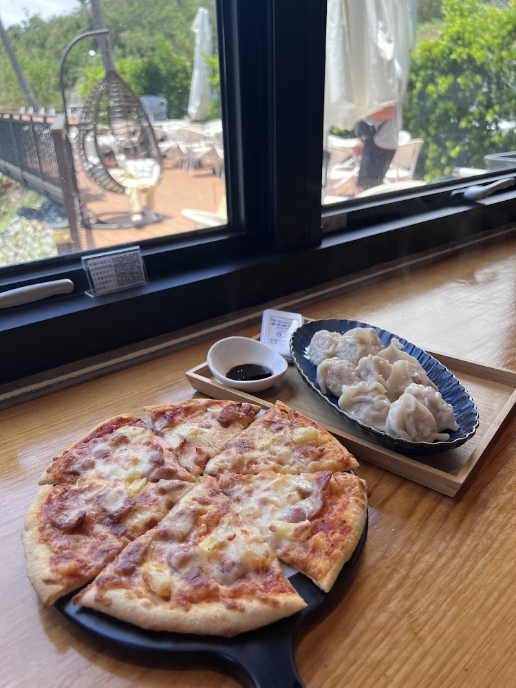 夏威夷比薩、一盤水餃和一小碟醬油，餐點擺放在窗邊的木桌上