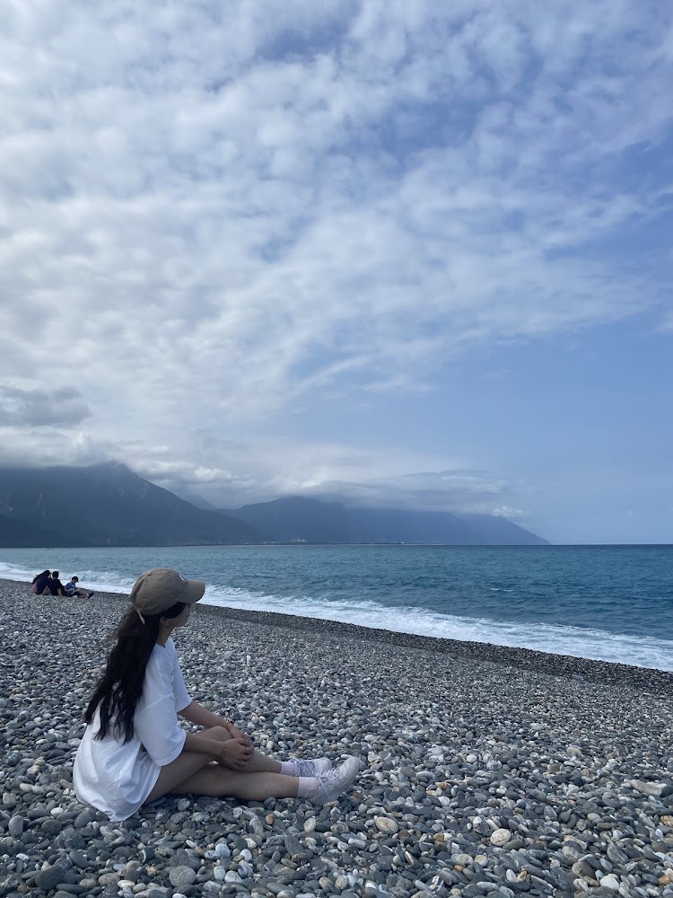 女孩坐在七星潭鵝卵石海灘上看海